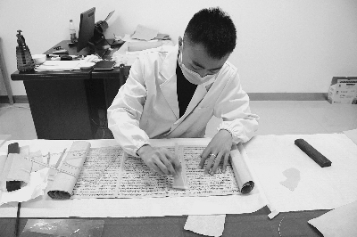 工作人员在对《敦煌写经》进行科学修复（敦煌市档案馆供图）